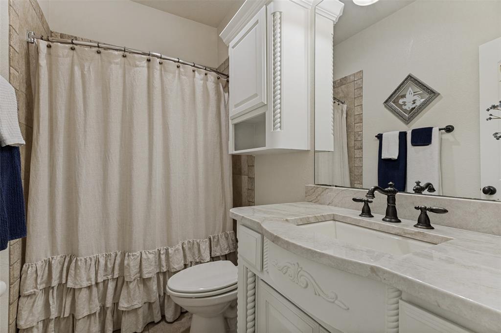 229 Arbor Lane Haslet, TX 76052 - Photo 22 of 34 Bathroom featuring a built-in vanity with a light-toned countertop and integrated sink, dark-toned faucet, wall-mounted mirror, and white cabinetry
