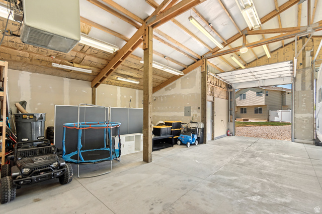 4752 South 4075th Street West Roy, UT 84067 - Photo 24 of 28 Spacious garage with exposed wood beam ceiling, concrete flooring, fluorescent lighting, and a large roll-up door