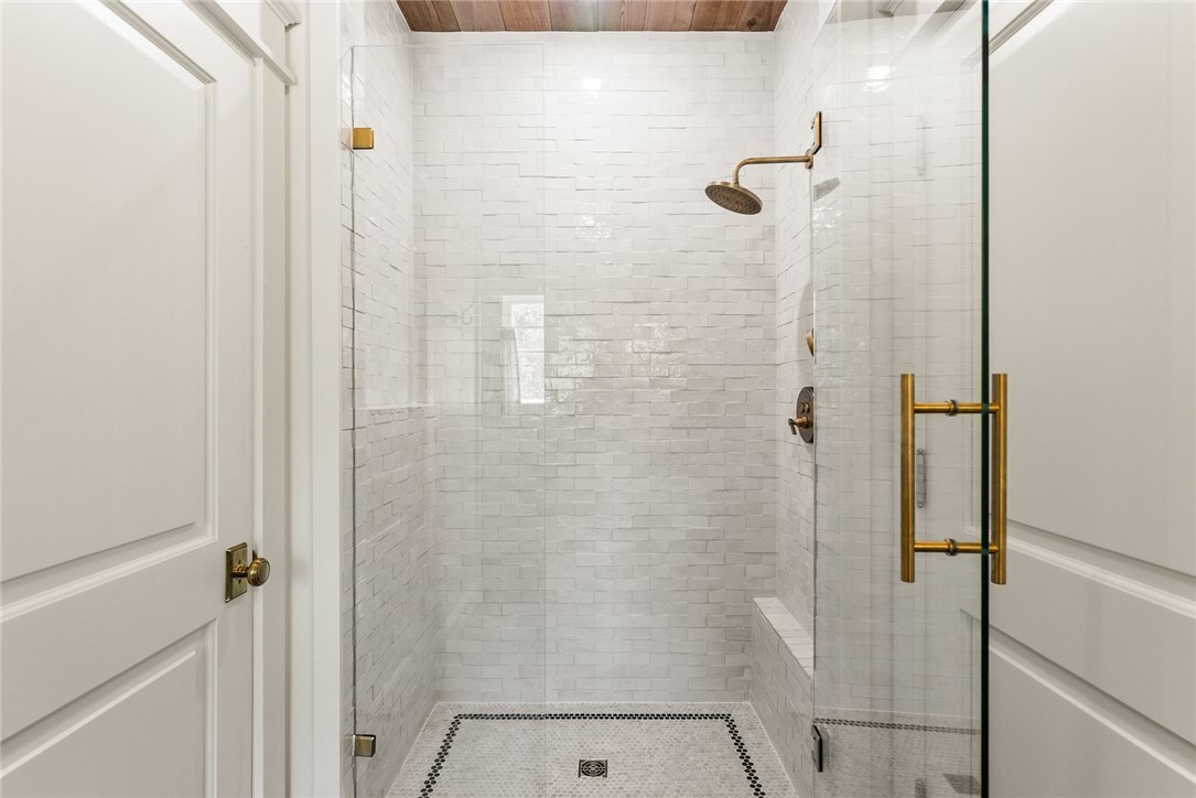 425 Barnhardt Road Timbo, AR 72680 - Photo 39 of 60 Walk-in shower featuring a glass enclosure with brass-finish hardware, textured white subway tile surround, integrated shower bench, and a mosaic tile floor with a decorative border