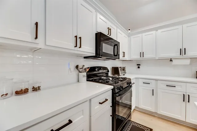 a view of a kitchen with white cabinets and black appliances