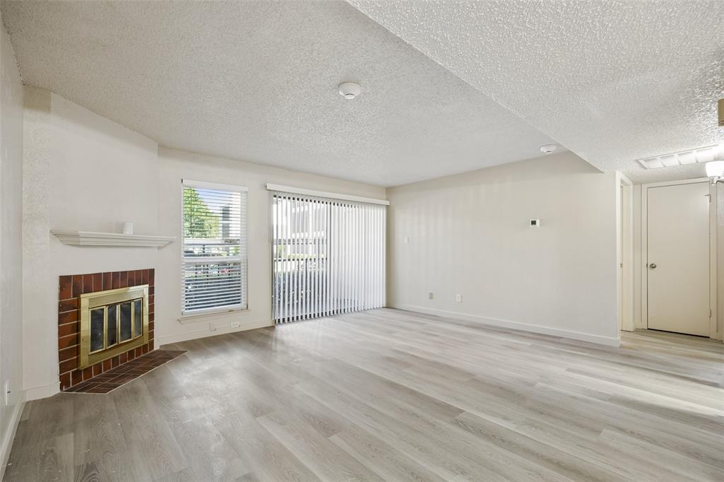 11480 Audelia Road, Unit 136 Dallas, TX 75243 - Photo 2 of 29 Spacious living area featuring light wood-finish flooring, a brick fireplace with a mantel, and a large sliding glass door with vertical blinds