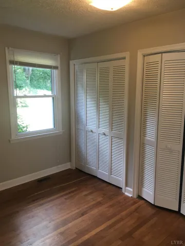 an empty room with wooden floor closet and windows