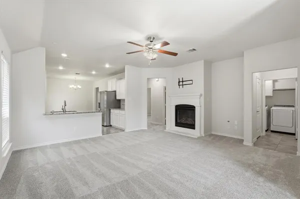 a view of a livingroom with a fireplace a ceiling fan and kitchen view