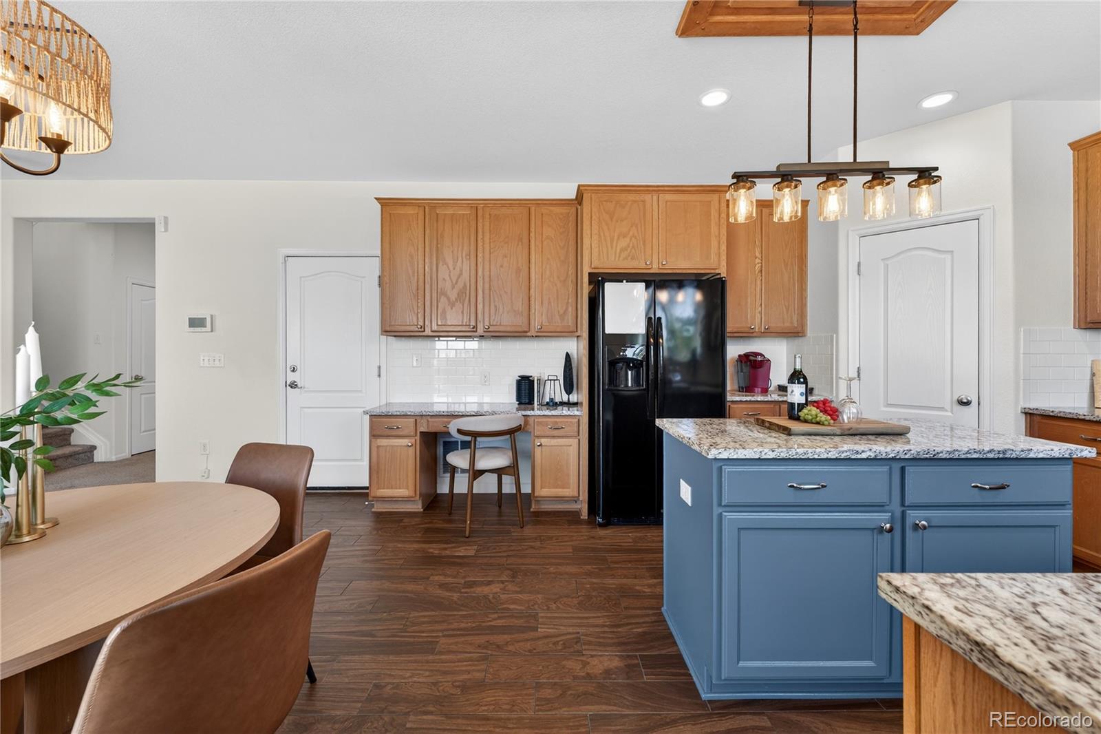 10180 Audrey Street Firestone, CO 80504 - Photo 17 of 46 a kitchen with granite countertop a refrigerator a stove a dining table and chairs with wooden floor