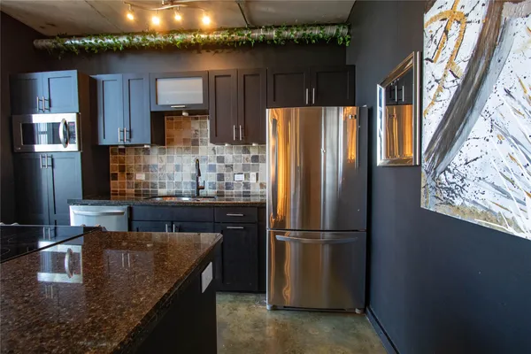 a kitchen with granite countertop a refrigerator a stove and a sink with wooden floor