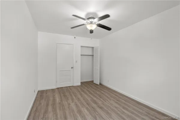 a view of an empty room with wooden floor and a ceiling fan