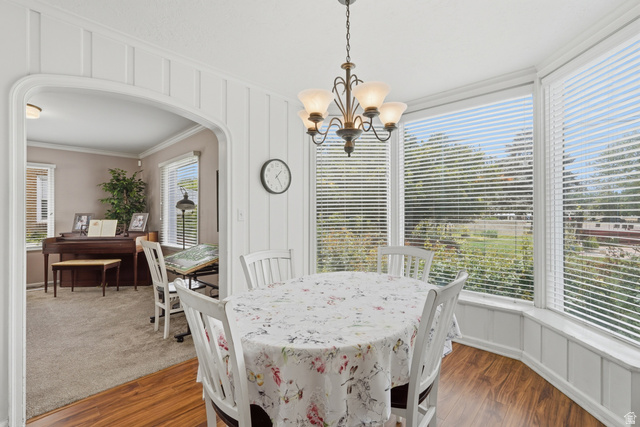 7576 South Jefferson Street Midvale, UT 84047 - Photo 10 of 53 Dining space featuring wood-finish flooring, a multi-pane bay window, white paneling, and an overhead chandelier