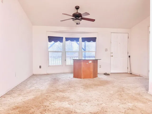 an empty room with chandelier fan and windows