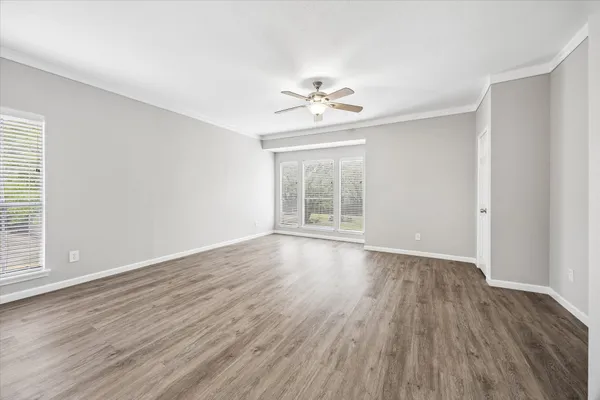 an empty room with wooden floor chandelier fan and windows