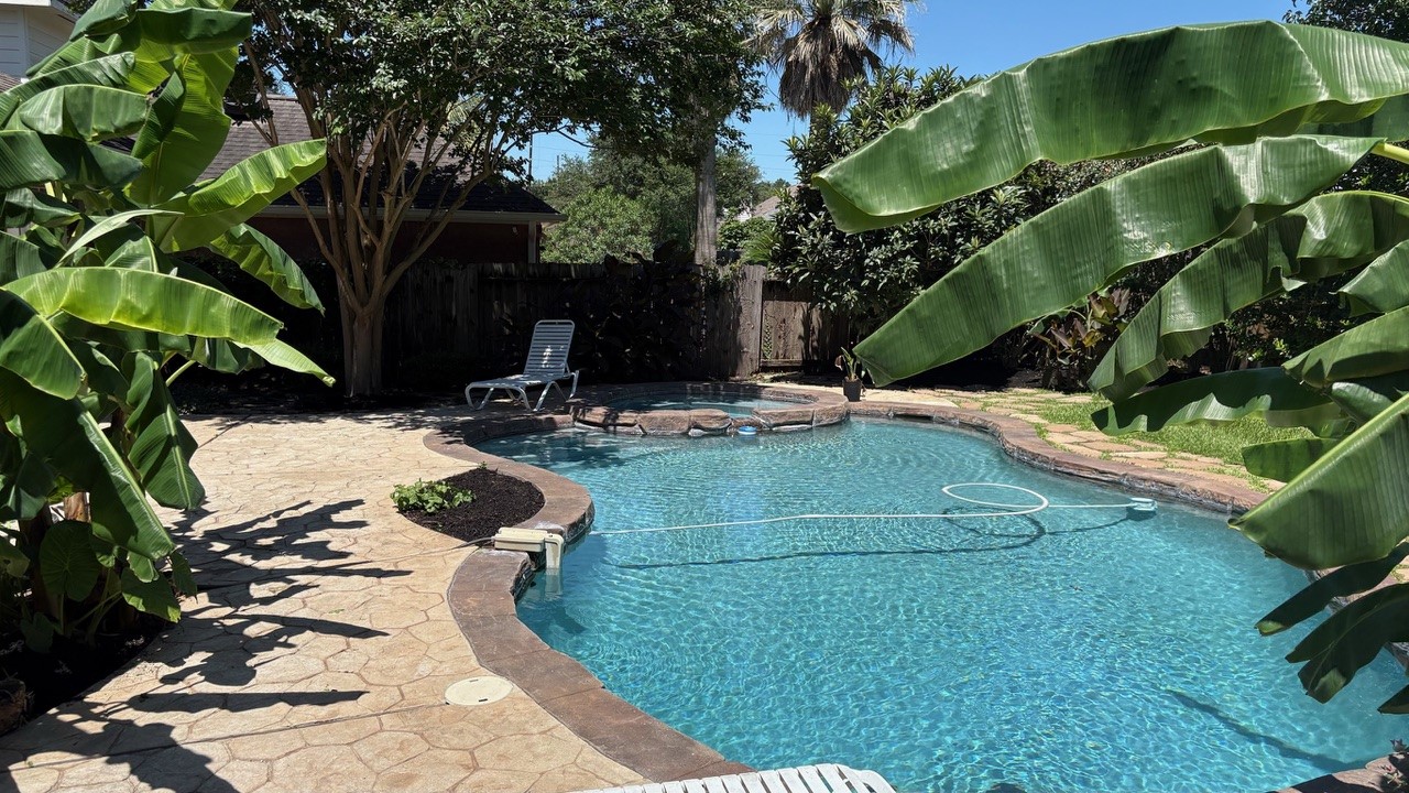 22402 Rue Canyon Court Katy, TX 77450 - Photo 15 of 18 Step out into a backyard paradise designed for ultimate relaxation. This sparkling, freeform swimming pool is surrounded by lush, mature banana trees and vibrant greenery, creating a natural screen for maximum privacy. The expansive stamped concrete decking offers plenty of room for poolside lounging, sunbathing, or hosting summer gatherings.