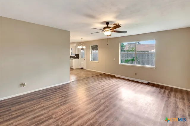 an empty room with wooden floor chandelier fan and windows