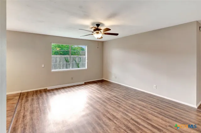 a view of an empty room with wooden floor and a window