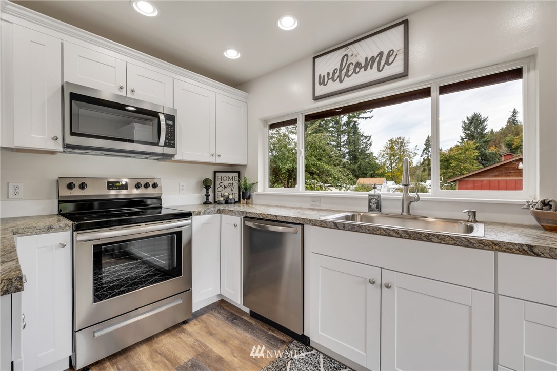 20260 Maxwell Road Southeast Maple Valley, WA 98038 - Photo 11 of 38 a kitchen with stainless steel appliances granite countertop a sink a stove a microwave and wooden cabinets