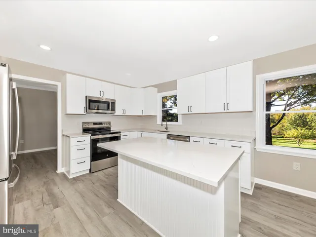 a kitchen with stainless steel appliances a stove a sink dishwasher a refrigerator with white cabinets and wooden floor