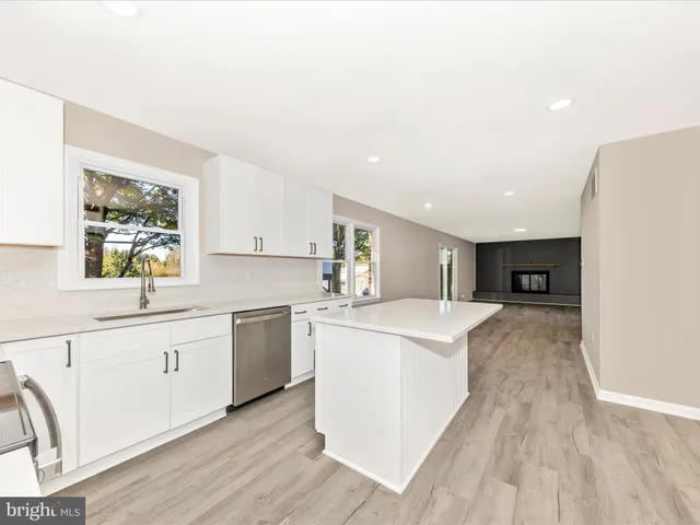 a large kitchen with stainless steel appliances granite countertop a stove a sink a refrigerator and white cabinets with wooden floor