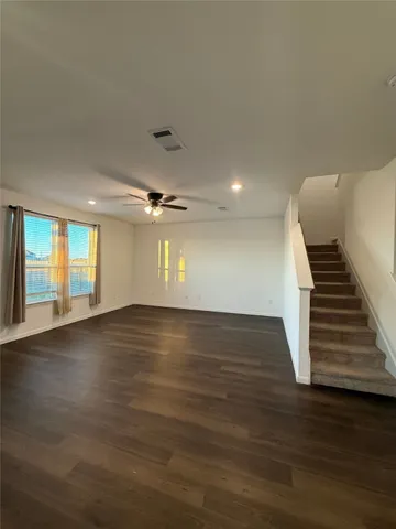 a view of an empty room with wooden floor and stairs