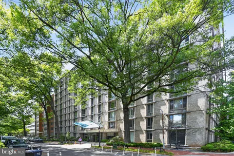 a front view of a building with lot of trees and plants