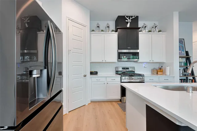 a kitchen with stainless steel appliances a refrigerator a sink and white cabinets