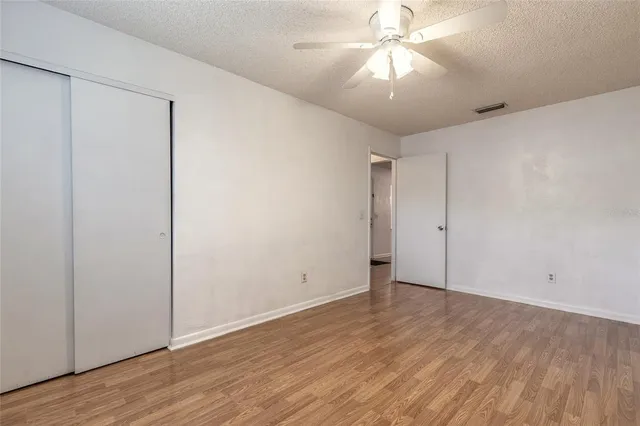 a view of an empty room with wooden floor and a ceiling fan