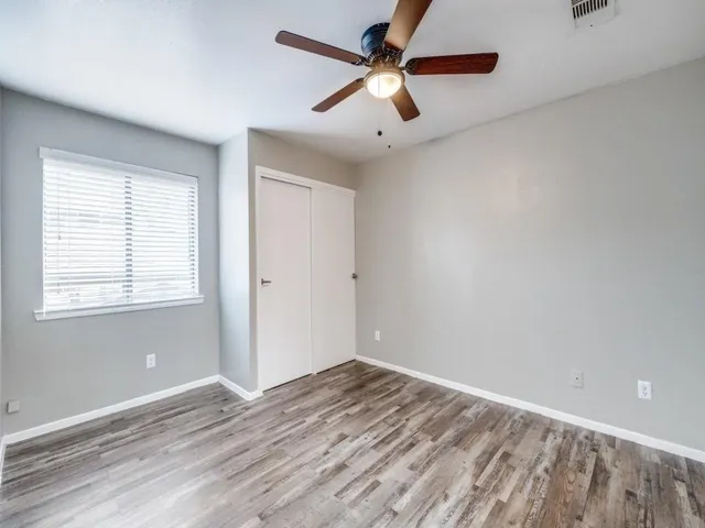 an empty room with wooden floor fan and windows