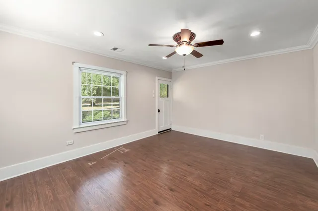an empty room with wooden floor chandelier fan and windows