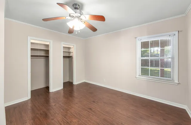 an empty room with wooden floor chandelier fan and windows