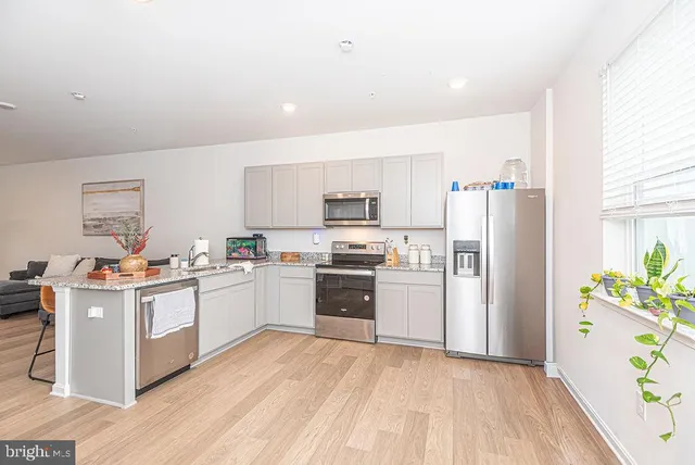 a kitchen with stainless steel appliances a stove a refrigerator a sink a microwave a refrigerator and white cabinets with wooden floor