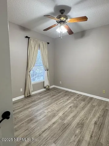 an empty room with wooden floor fan and window