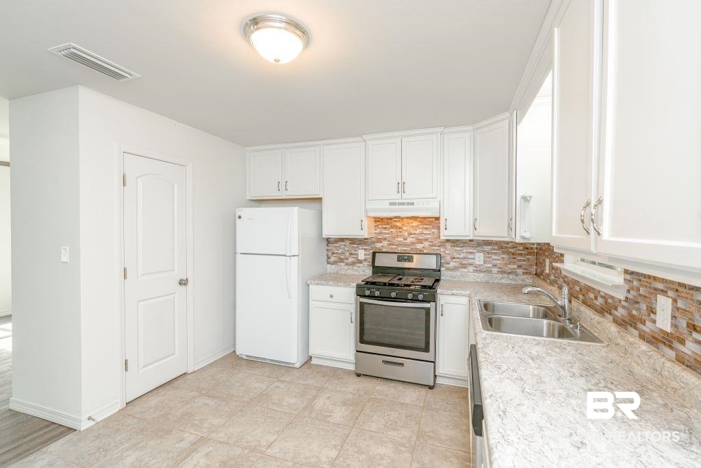 12641 Pecan Street Grand Bay, AL 36541 - Photo 9 of 23 Kitchen featuring white cabinets, sink, decorative backsplash, stainless steel gas range oven, and white fridge
