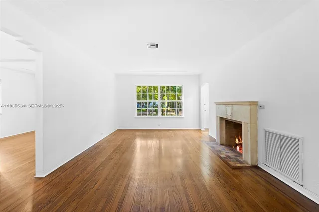 an empty room with wooden floor fireplace and windows