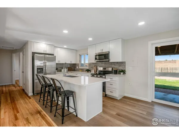 a open kitchen with stainless steel appliances granite countertop a refrigerator a stove top oven a sink dishwasher and white cabinets with wooden floor