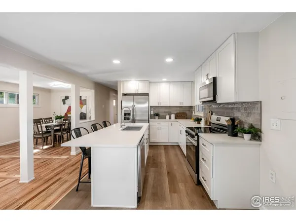 a kitchen with stainless steel appliances kitchen island granite countertop a refrigerator oven a sink dishwasher and white cabinets with wooden floor