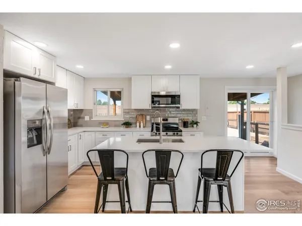 a kitchen with stainless steel appliances granite countertop a dining table chairs refrigerator and microwave