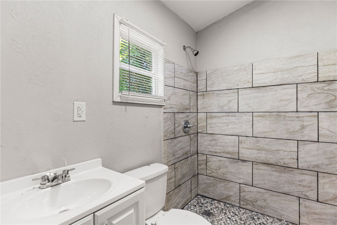 109 Farmer Street Anderson, SC 29621 - Photo 18 of 31 A well-lit bathroom features a vanity, toilet, and a tiled shower with a pebble-stone floor.