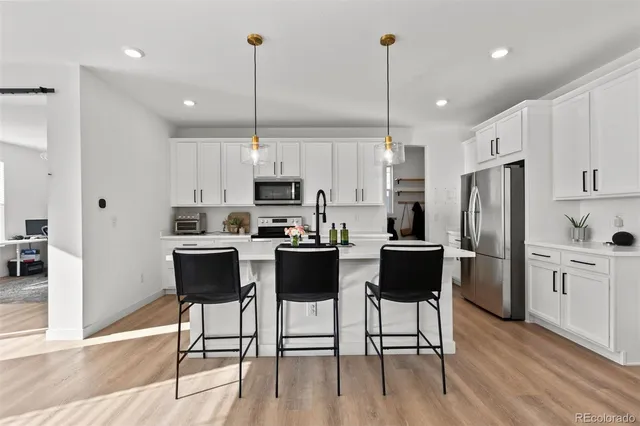 a kitchen with kitchen island granite countertop a refrigerator a stove a sink a dining table and chairs with wooden floor