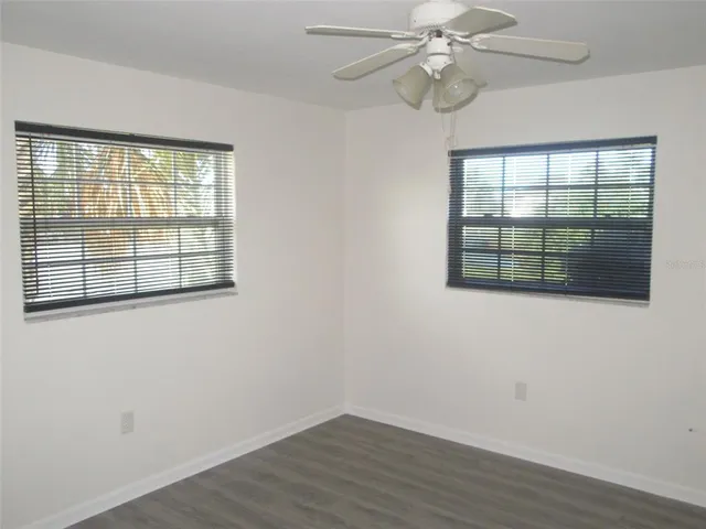 an empty room with wooden floor chandelier fan and windows