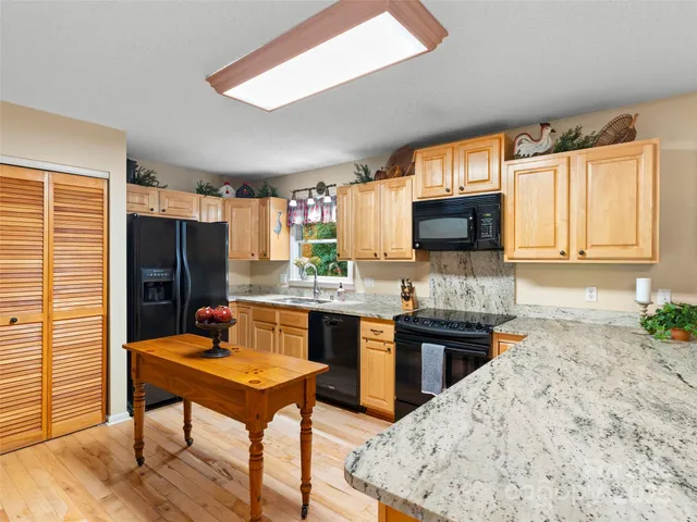 a kitchen with stainless steel appliances granite countertop a stove top oven a sink dishwasher a dining table and chairs with wooden floor