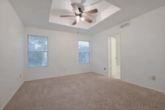 an empty room with a chandelier fan and windows