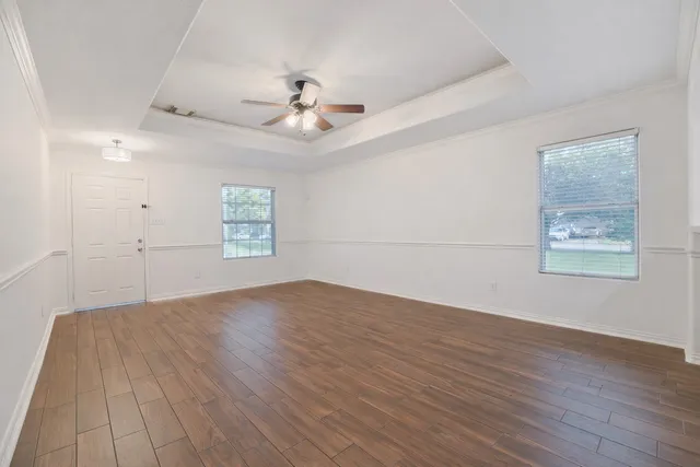 an empty room with wooden floor chandelier fan and windows