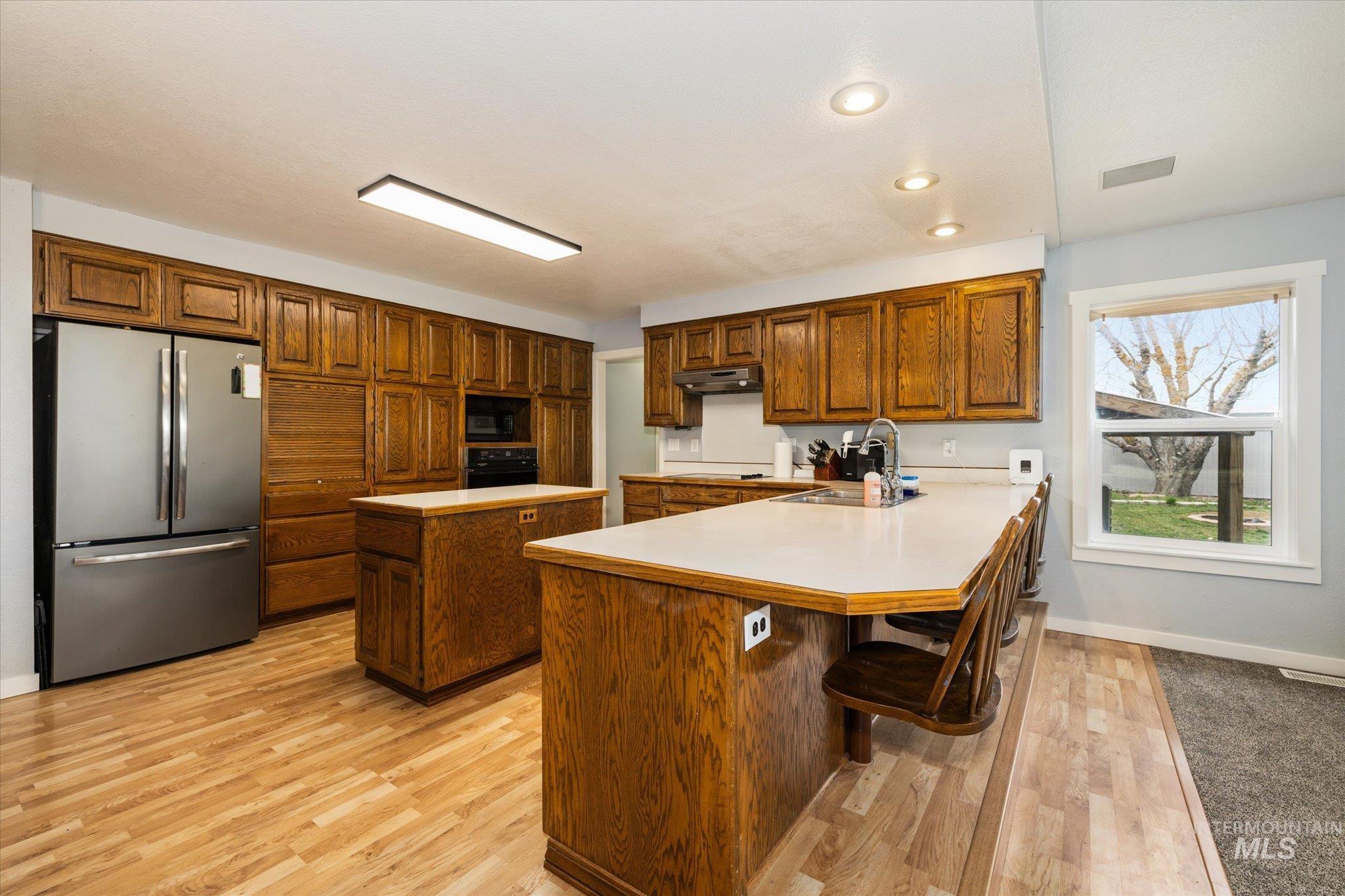 15032 Hollow Road Caldwell, ID 83607 - Photo 22 of 50 Kitchen featuring wood finish cabinetry, freestanding refrigerator, light countertops, a breakfast bar area, and light wood-type flooring