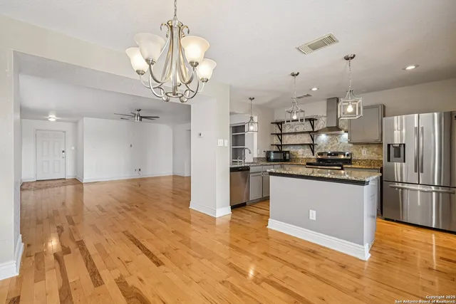 a kitchen with stainless steel appliances granite countertop a refrigerator a sink dishwasher a stove and a dining table with wooden floor