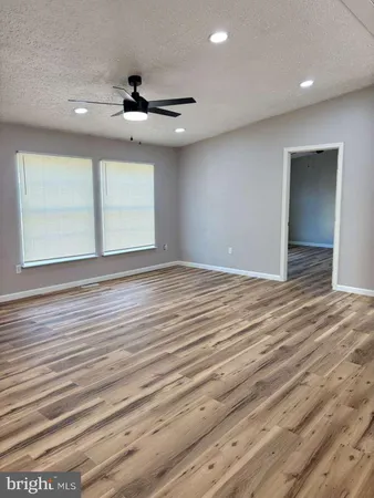 an empty room with wooden floor ceiling fan and windows