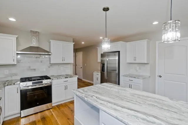 a kitchen with stainless steel appliances kitchen island granite countertop a stove a sink dishwasher a refrigerator and a wooden floor