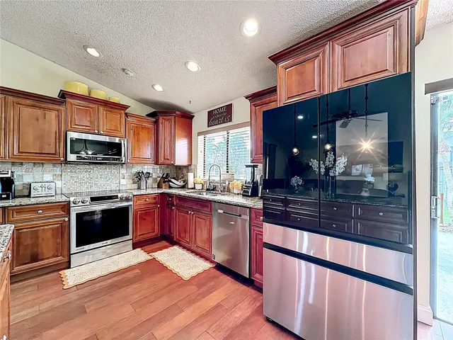 a large kitchen with stainless steel appliances granite countertop a large stove top oven a sink dishwasher a dining table and chairs with wooden floor