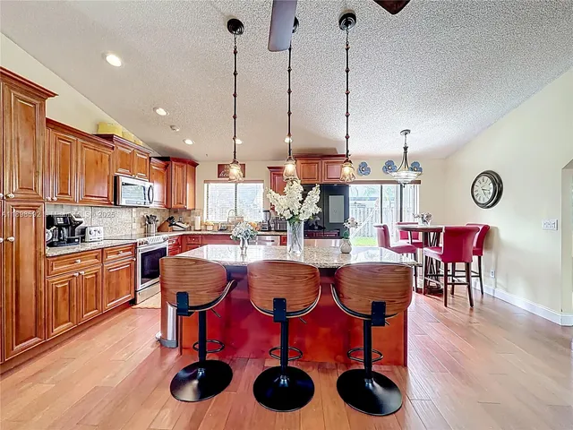 a view of kitchen with stainless steel appliances granite countertop a dining table chairs and white cabinets