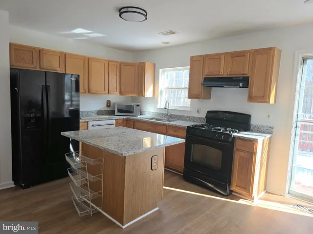 a kitchen with stainless steel appliances granite countertop a stove a refrigerator and a sink with wooden cabinets