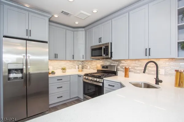 a kitchen with stainless steel appliances granite countertop a refrigerator a sink a stove a microwave and white cabinets