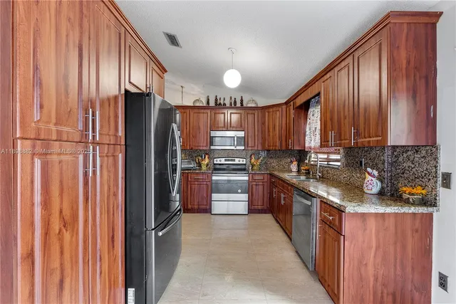 a kitchen with stainless steel appliances granite countertop a refrigerator a sink dishwasher a stove and a refrigerator with wooden cabinets