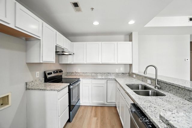 a kitchen with a sink dishwasher a stove top oven a refrigerator with white cabinets and wooden floor