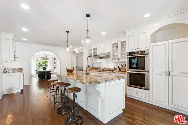 a kitchen with stainless steel appliances kitchen island granite countertop a stove a refrigerator a oven a dining table and chairs with wooden floor